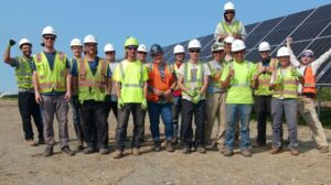 A group of people in visibility vests and hard hats poses in front of solar array.